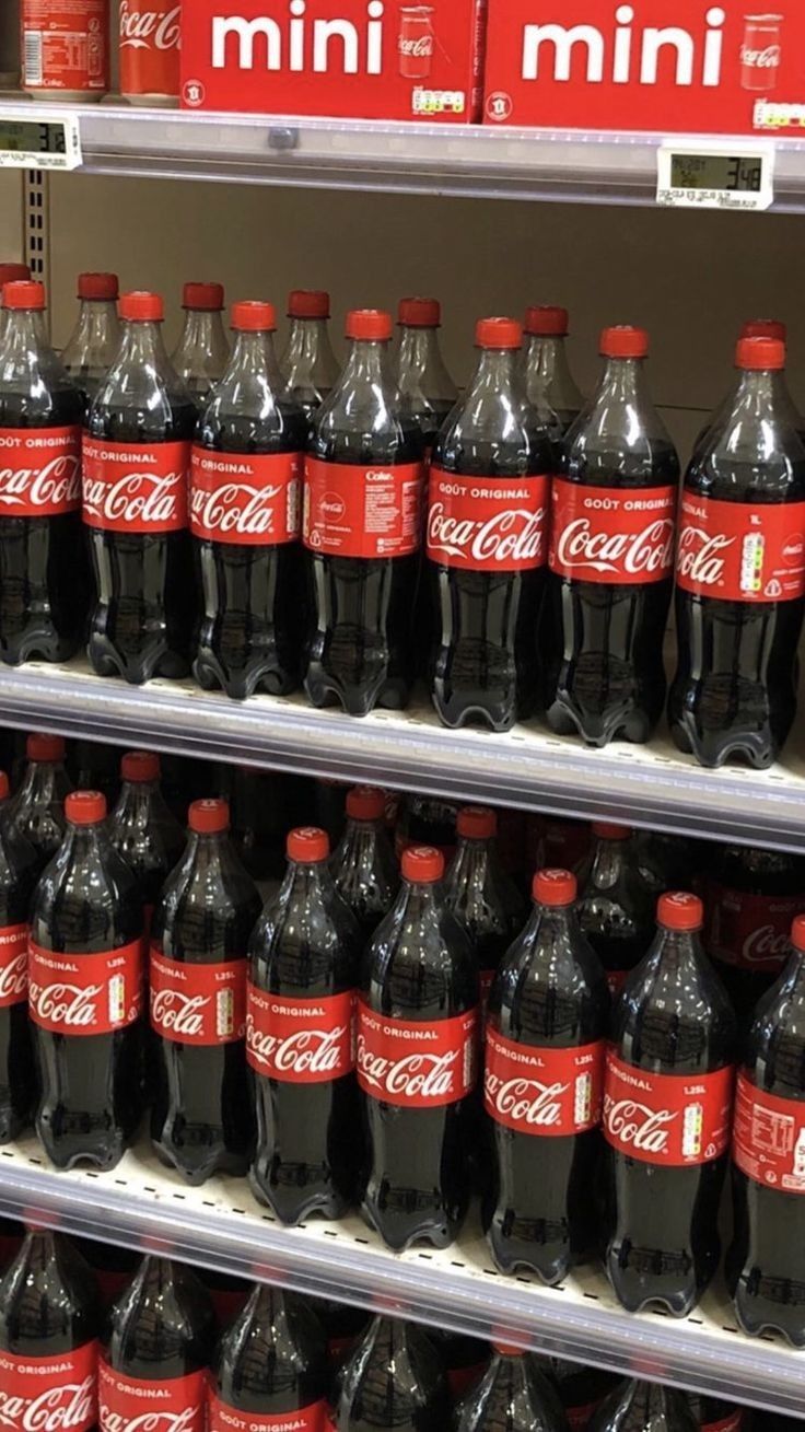 several bottles of coca - cola are on display in a grocery store, one is red and the other is black