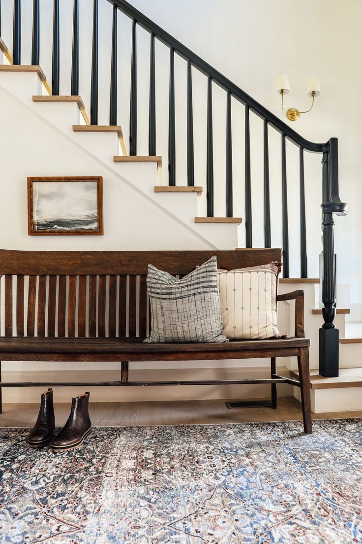 a wooden bench sitting under a stair case next to a bannister with pictures on it