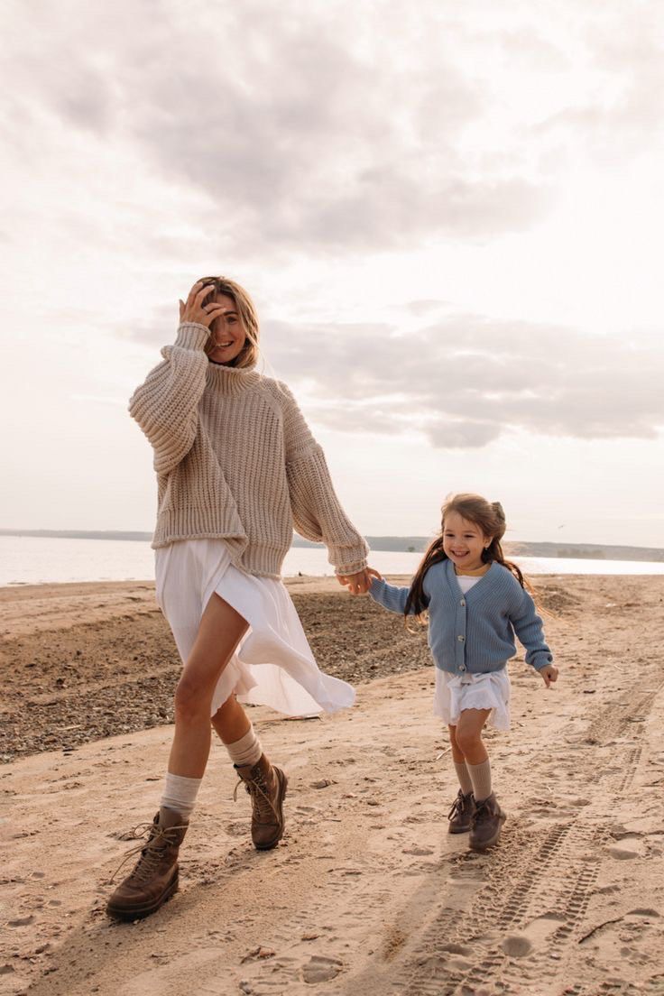 a mother and daughter walking on the beach holding hands