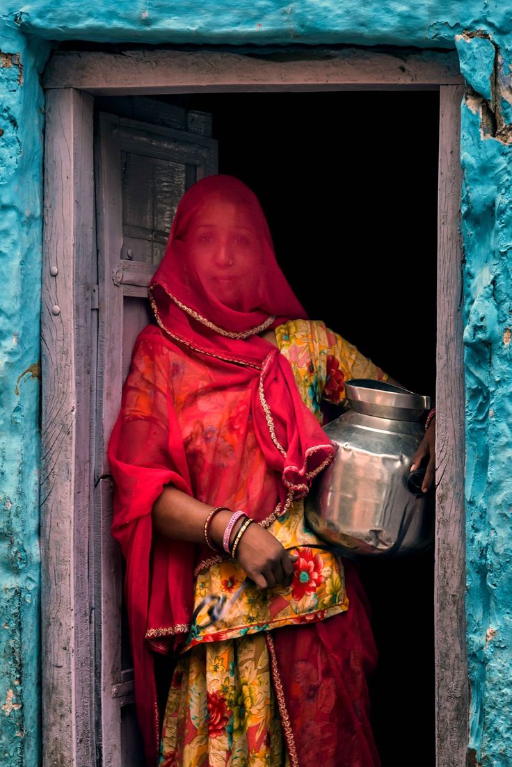 a woman in red is holding a pot and looking out the window with blue paint