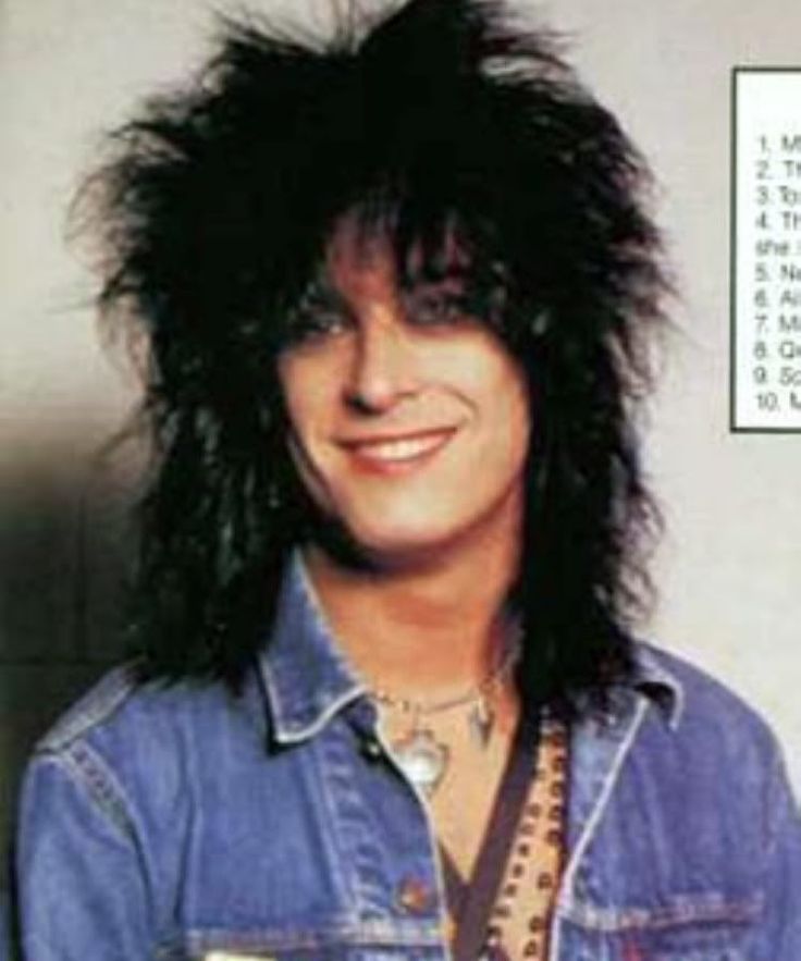 a man with long black hair wearing a denim shirt and holding a drink in his hand