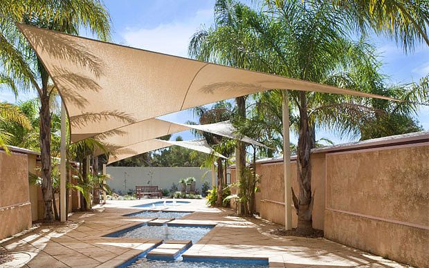 an outdoor swimming pool surrounded by palm trees and shade sails over it's sides