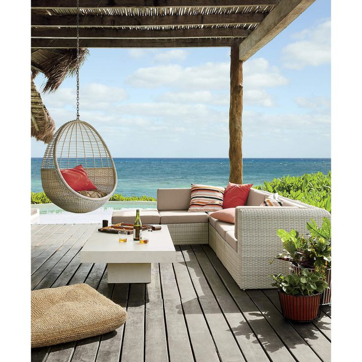 an outdoor living area overlooking the ocean with hanging chairs and couches on wooden decking