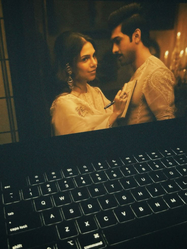 a man and woman standing next to each other in front of a laptop computer screen