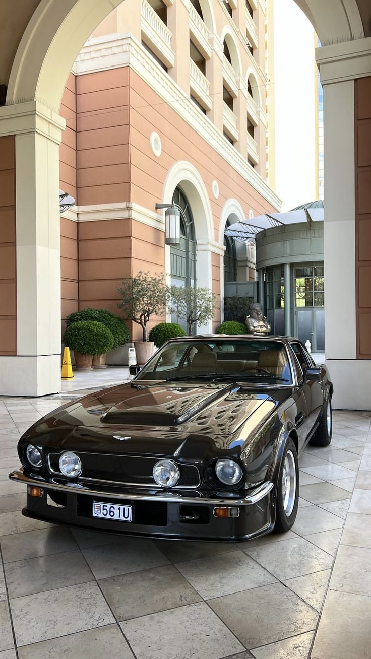 a black car parked in front of a tall building with an archway leading into it