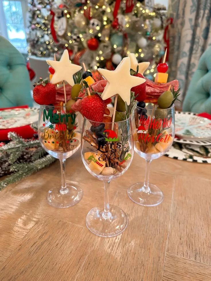 three wine glasses with strawberries and other food in them sitting on a table next to a christmas tree