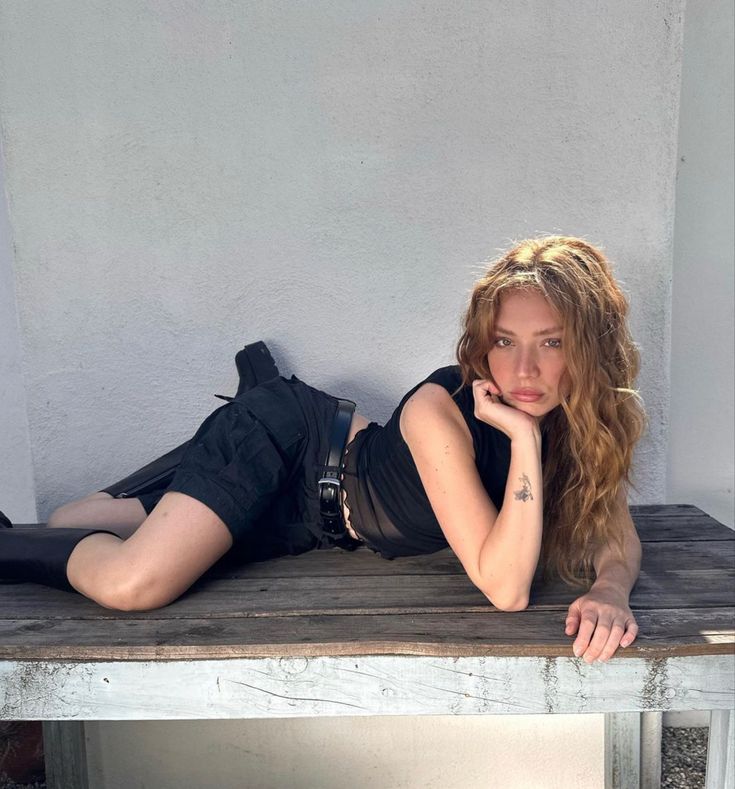 a beautiful young woman laying on top of a wooden bench