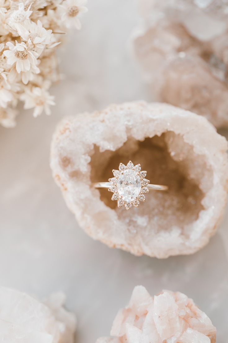 an engagement ring sitting on top of a piece of rock surrounded by flowers and crystals