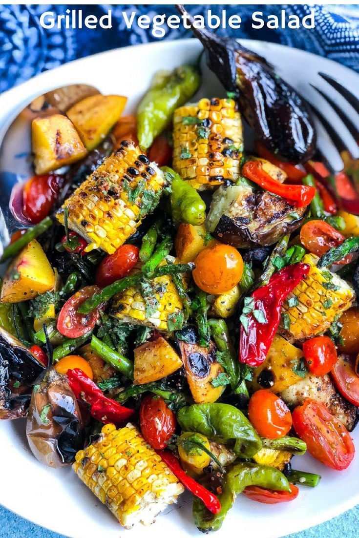 a white plate topped with grilled vegetables on top of a blue table cloth next to a fork