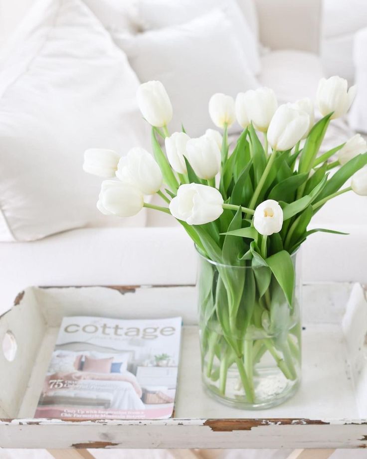 a glass vase filled with white tulips on top of a table