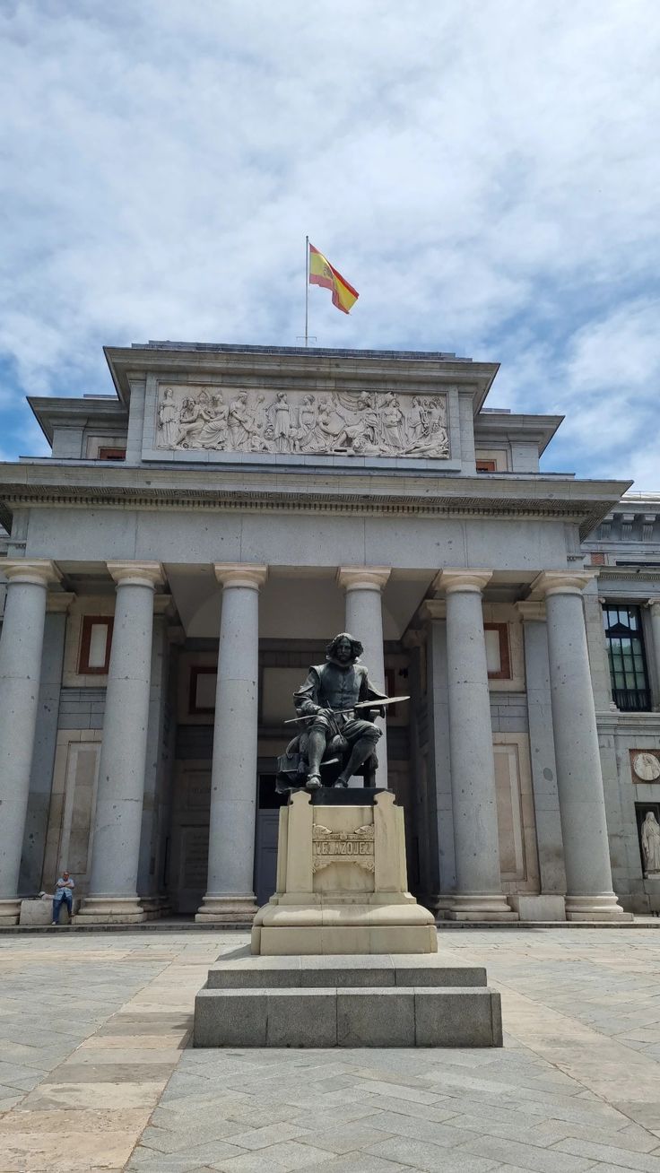 a statue in front of a large building with columns and a flag on top of it