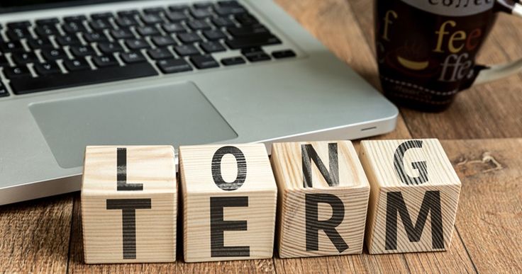 wooden blocks spelling the word long term next to a laptop