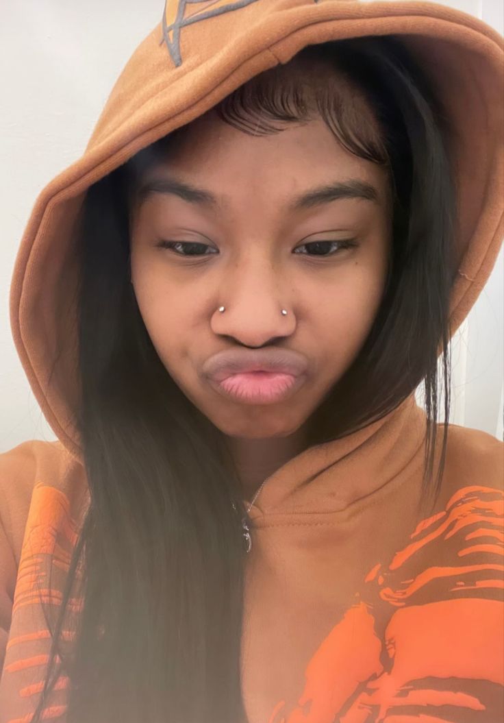 a girl with a nose piercing wearing an orange hoodie