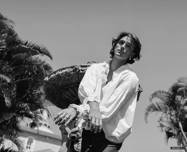 black and white photograph of a man holding a skateboard in front of palm trees