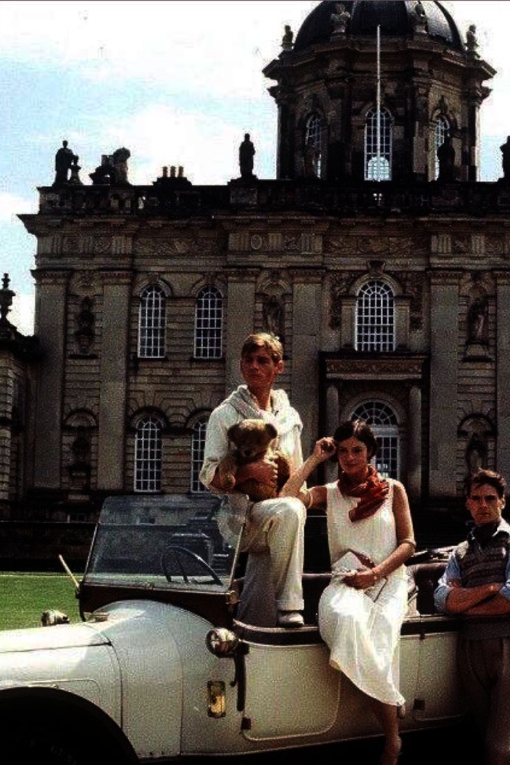 a group of people sitting on top of an old car in front of a large building