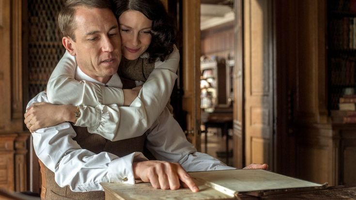 a man and woman embracing each other while sitting at a table with an open book