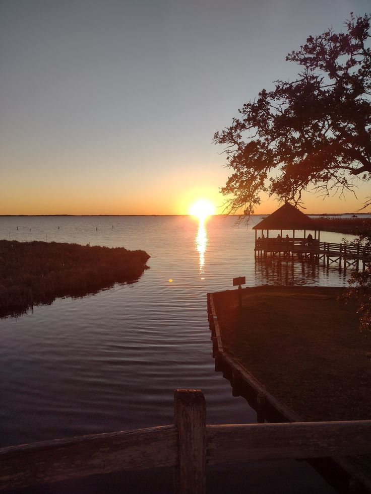 the sun is setting over the water near a dock