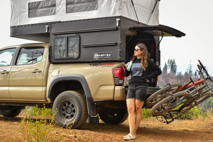 a woman standing next to her truck with bikes in the back and an off road camper