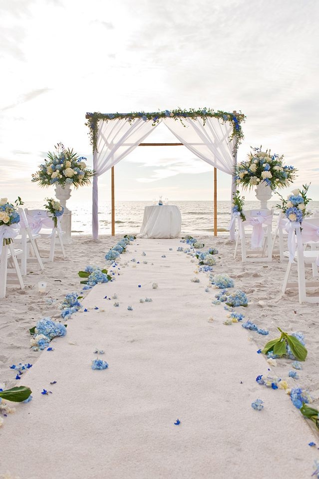 an outdoor wedding setup on the beach with blue flowers and white draping over the aisle