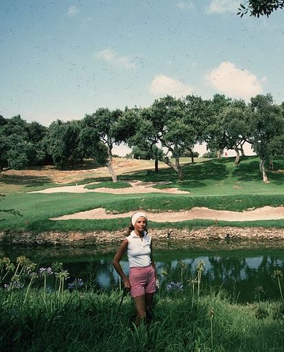 a man standing next to a pond on top of a lush green field near a golf course