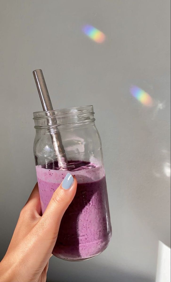 a hand holding a glass jar filled with pink and purple liquid next to a white wall