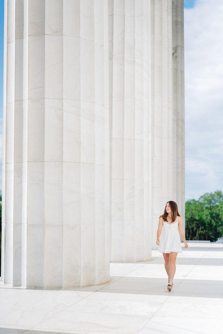 a woman in a white dress is walking by the columns