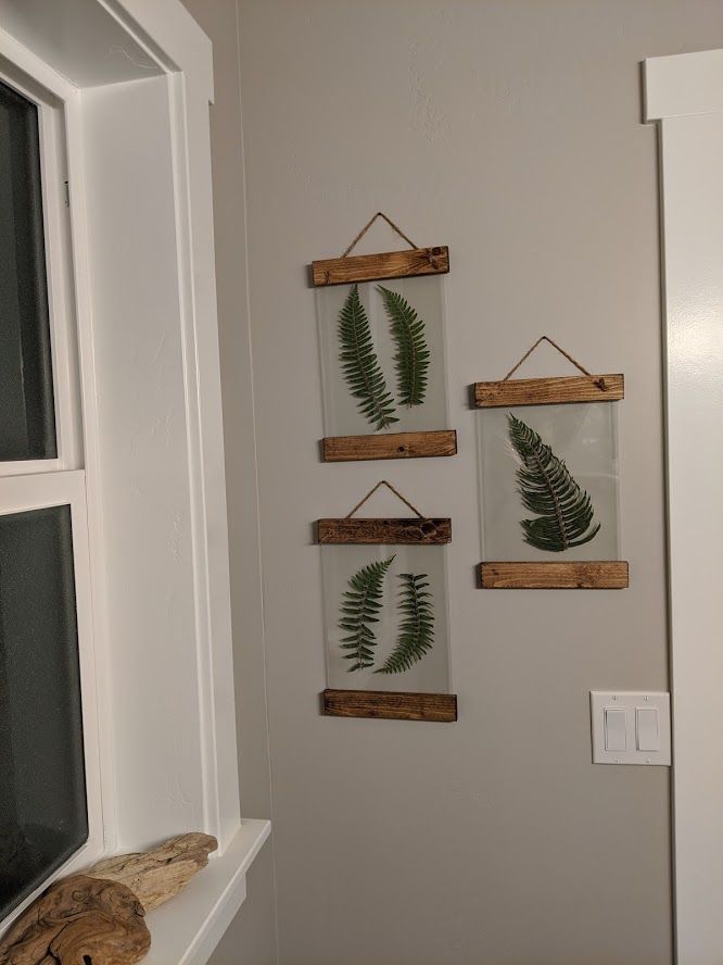 three wooden frames hanging on the wall with green leaves in them and a teddy bear next to it