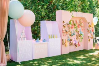 an outdoor party with balloons and decorations on the grass, in front of a pink backdrop