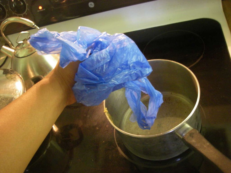 a person holding a plastic bag over a pot on the stove with water in it