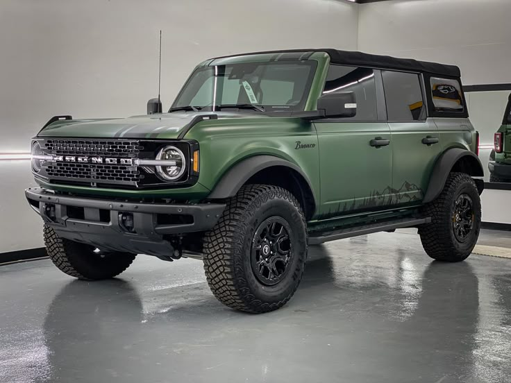 a green truck parked in a garage next to another vehicle with black tires on it