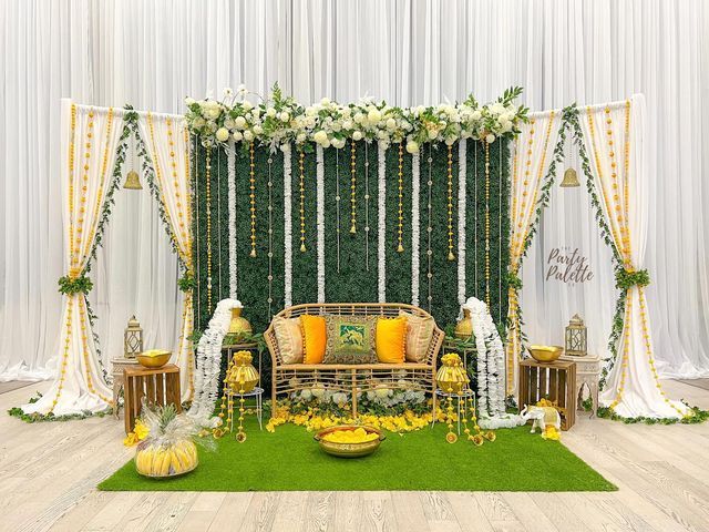 a wedding stage decorated with flowers, greenery and yellow pillows for the bride's seating