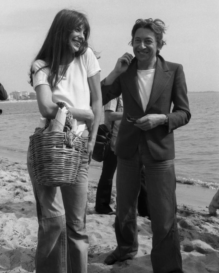 black and white photograph of two people standing on the beach, one holding a basket