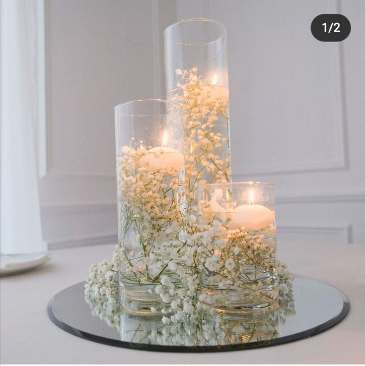 there are candles in glass vases with flowers on the table next to each other