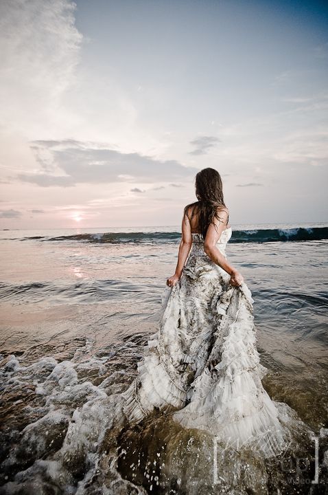 a woman is standing in the water at the beach with her dress flowing over her body