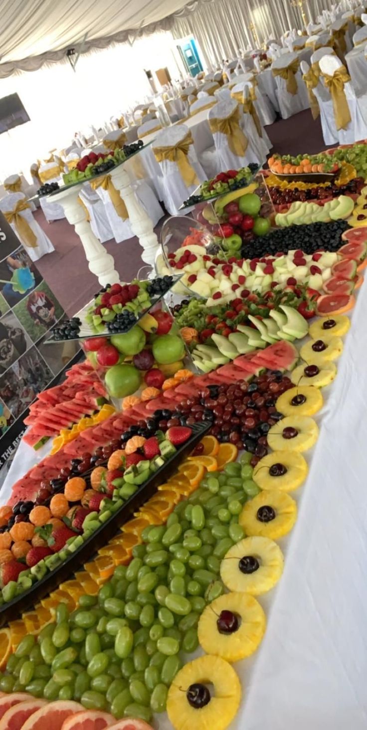 many different types of fruits on display at a buffet table with white linens and yellow ribbons