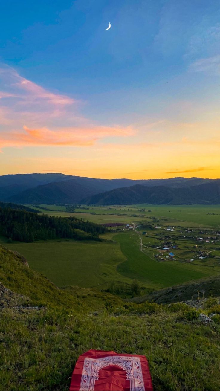 a blanket is laying on the ground in front of a beautiful sunset over a valley