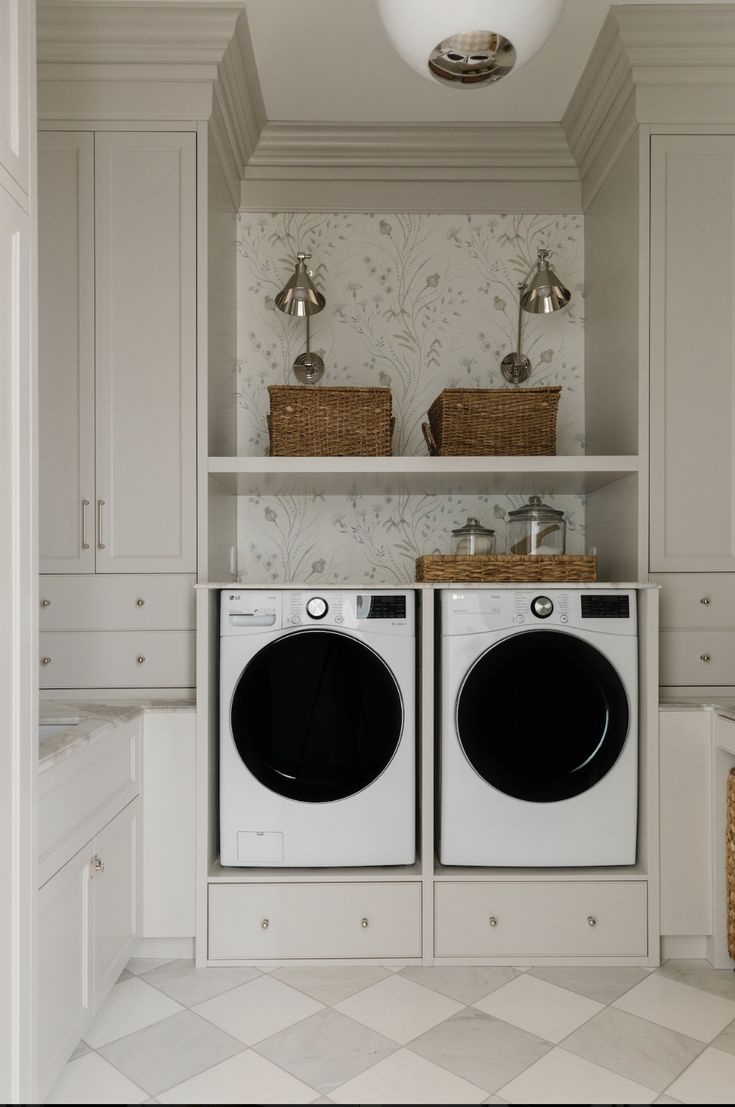 a washer and dryer in a white laundry room with wall - to - wall cabinets