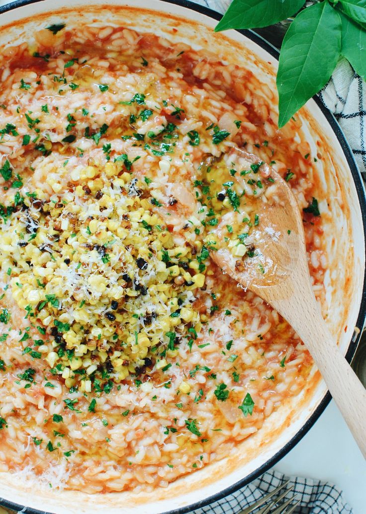 a large pot filled with lots of food on top of a table next to a wooden spoon