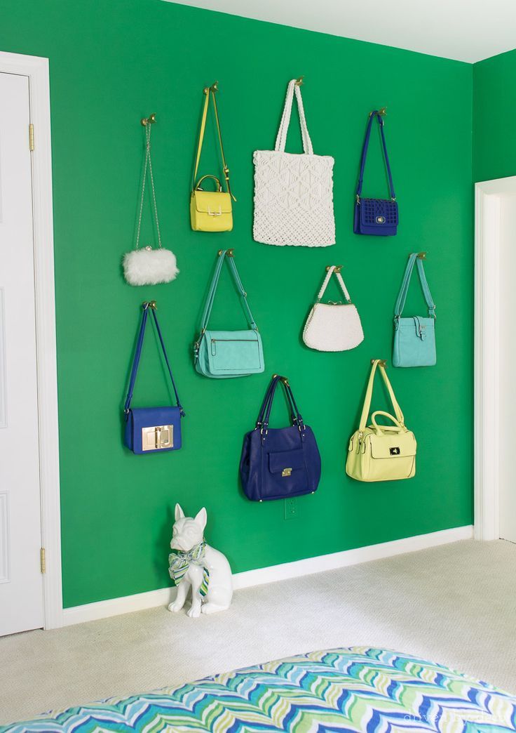 a green wall with purses hanging on it and a small white dog sitting in the foreground