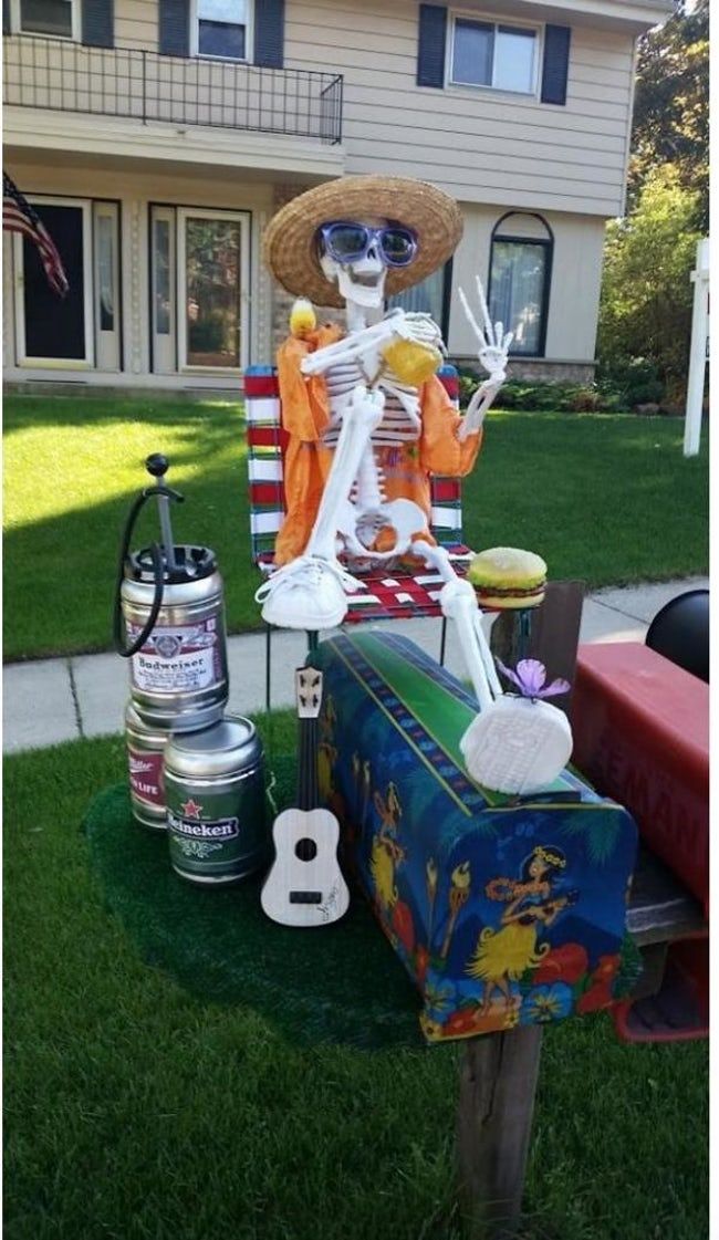 a skeleton sitting on top of a mailbox in the grass next to a house