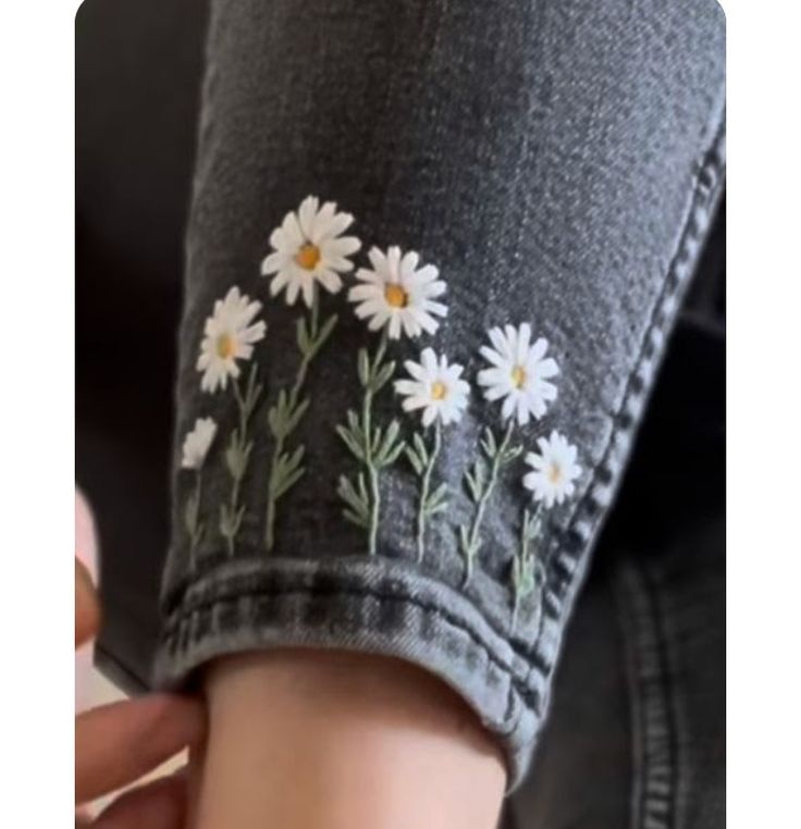 a woman's arm with white daisies embroidered on the back of her jeans