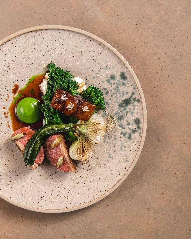 a white plate topped with meat and veggies on top of a brown table