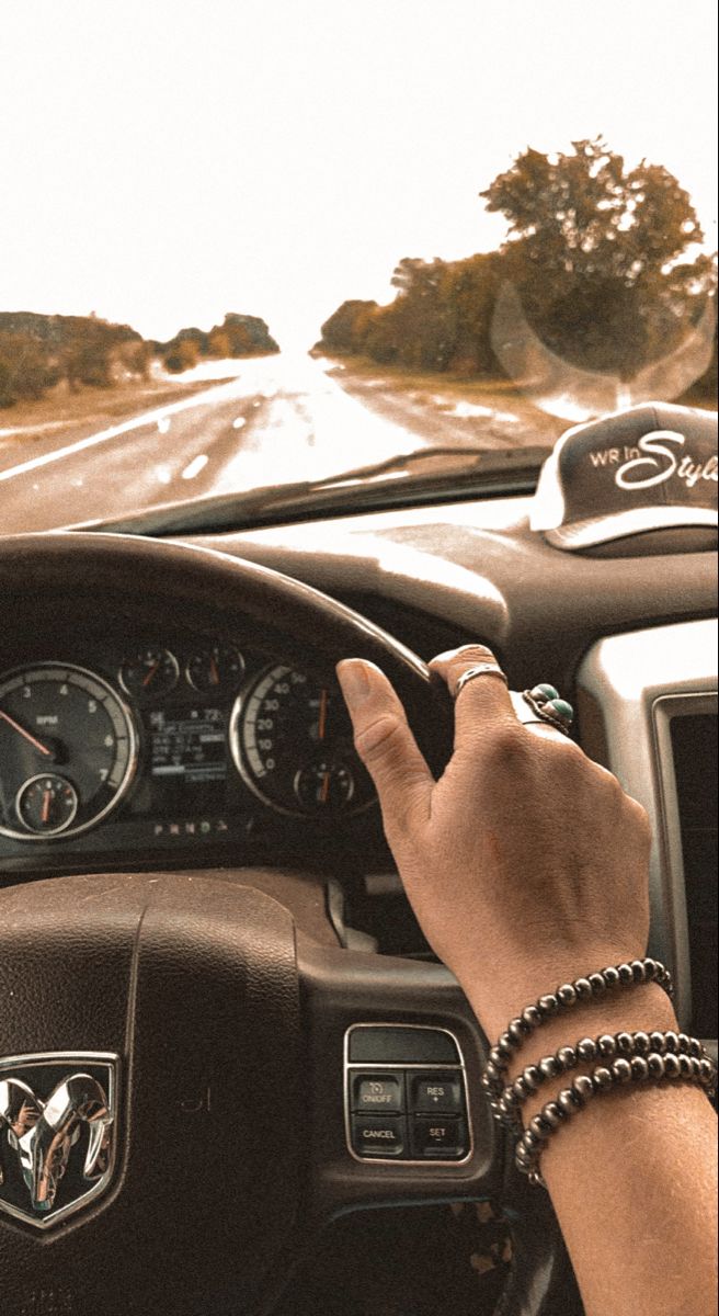 a person driving a car down a road with their hand on the steering wheel and dashboard