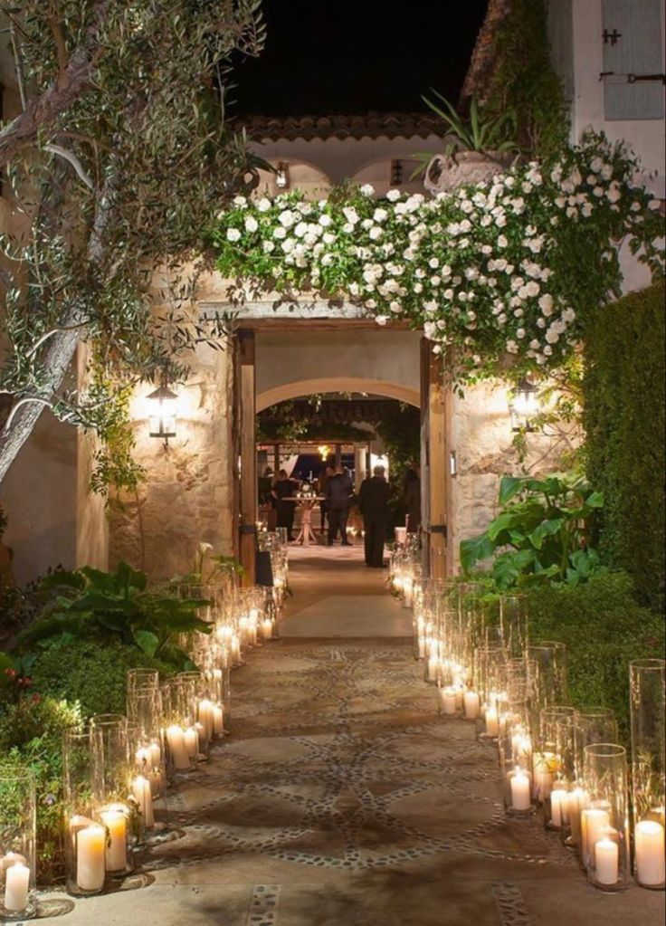 candles are lit in front of an entrance to a house with white flowers and greenery