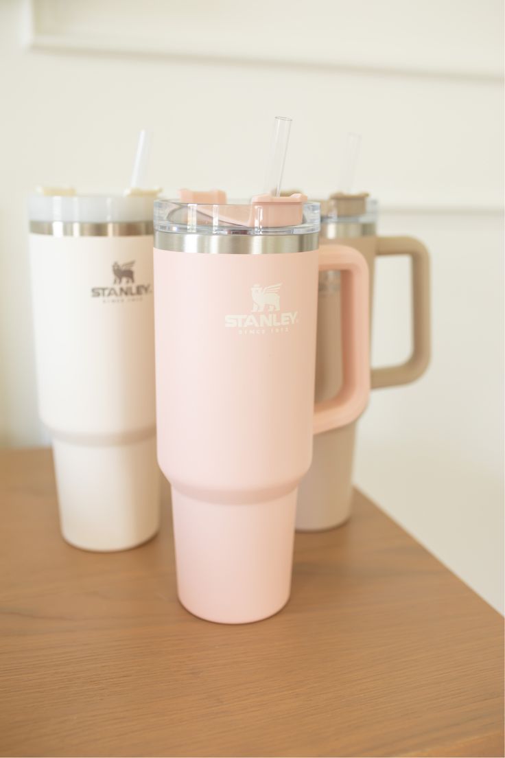 three coffee mugs sitting on top of a wooden table with straws in them