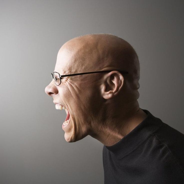 an old man screaming with his mouth wide open in front of the camera on a gray background