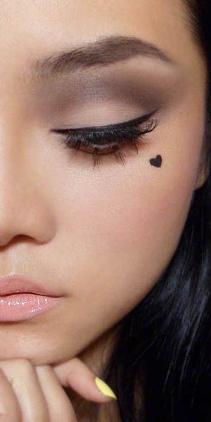 a woman with her hand on her chin looking down at her eyeliner and makeup