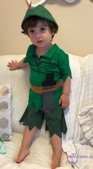 a little boy dressed up as peter the neverland elf sitting on top of a bed