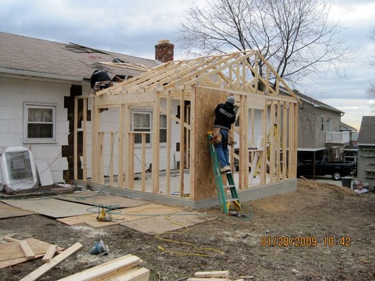 a man standing on top of a wooden frame in front of a house under construction