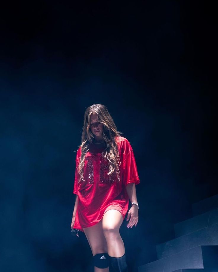 a woman in thigh high boots and a red shirt is standing on stage with her legs spread out